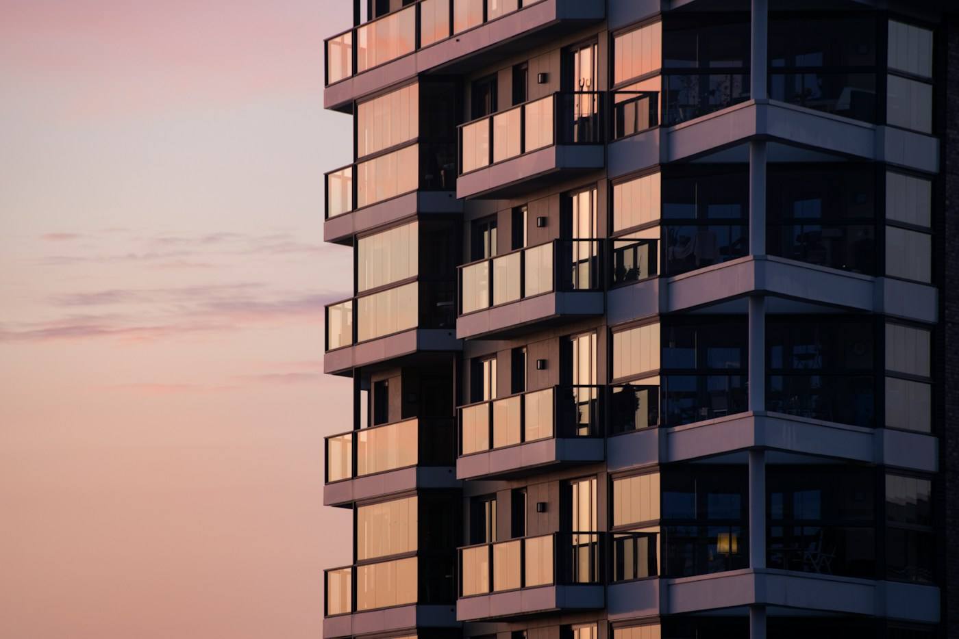 Fachada de um edifício residencial alto, com varandas de vidro, ao entardecer.