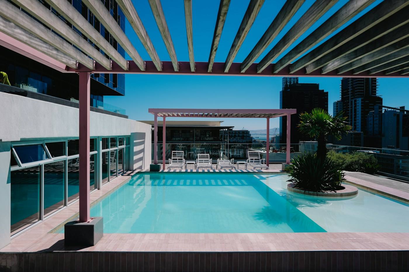 Piscina na cobertura de um prédio, com pergolado de madeira e espreguiçadeiras.